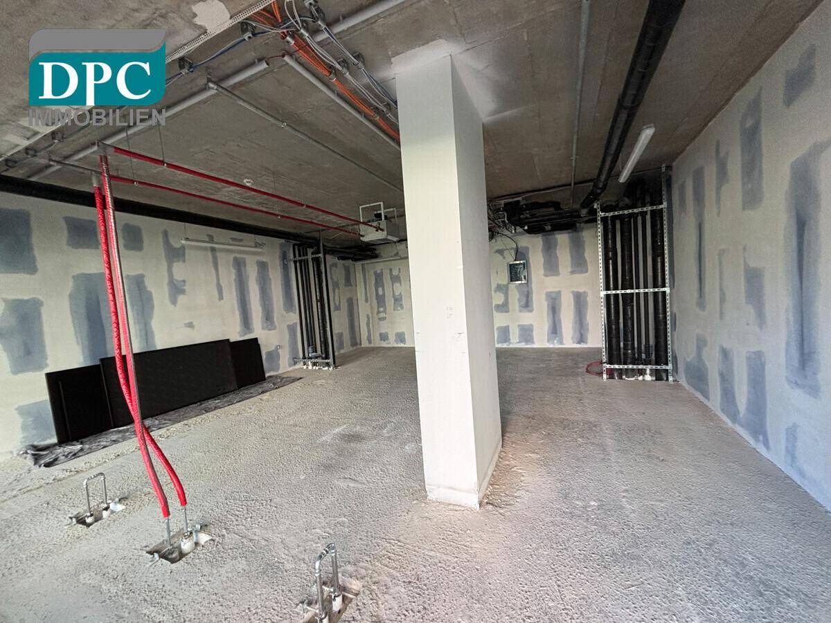 Unfertiger Gewerberaum mit sichtbaren Installationen, Betonboden und teilweise verputzten Wänden.
