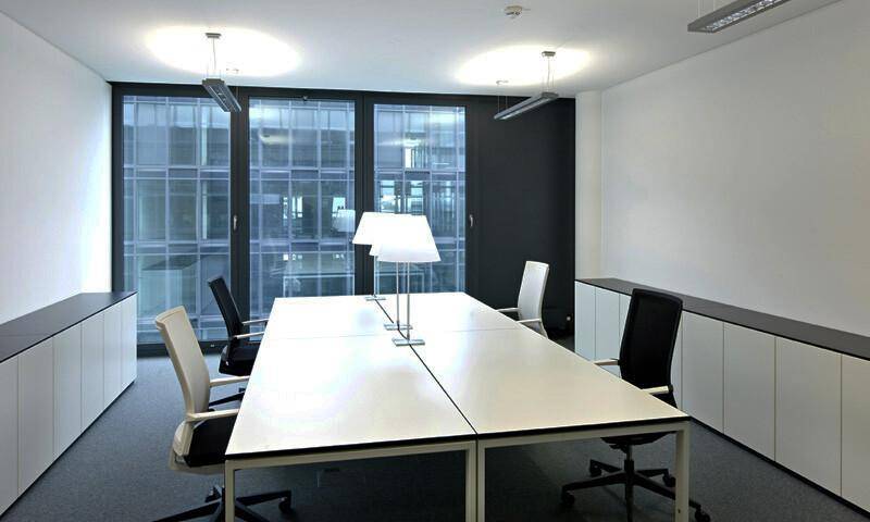 Konferenzraum mit großem Tisch, Bürostühlen und Blick auf die moderne Glasfassade des Gebäudes.