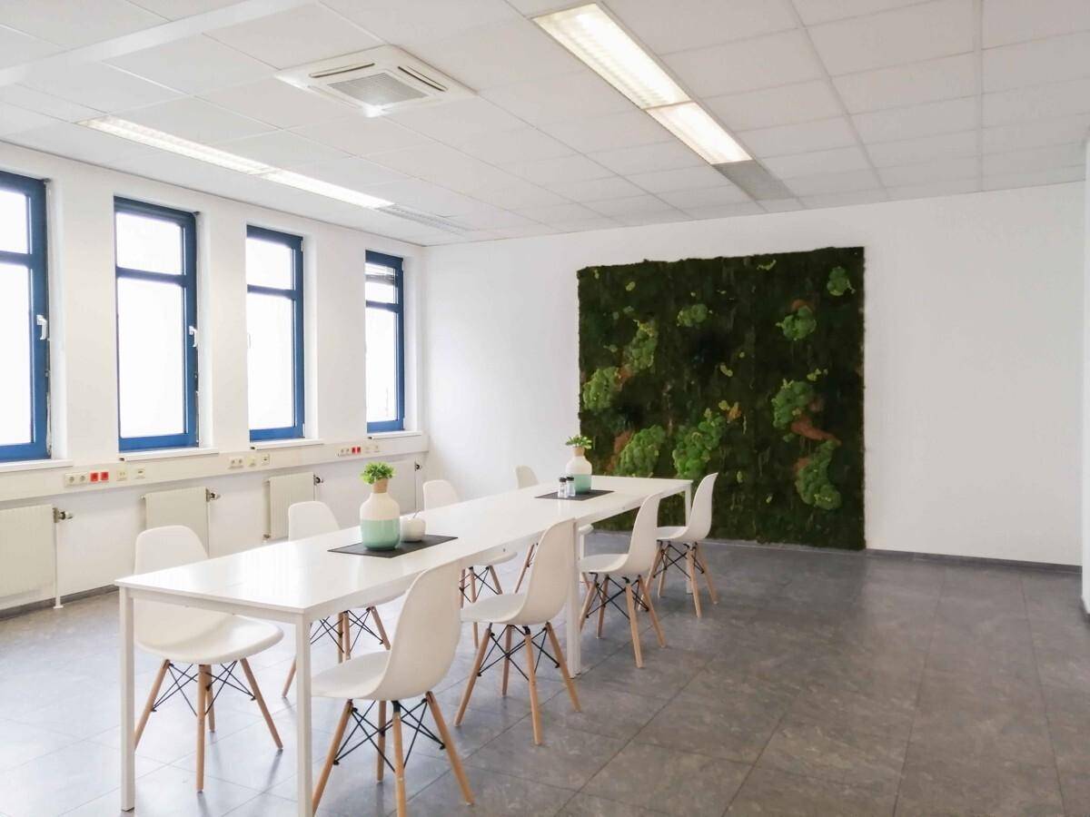 Heller Konferenzraum mit Fliesenboden, langer Tafel und einer großen Mooswand.