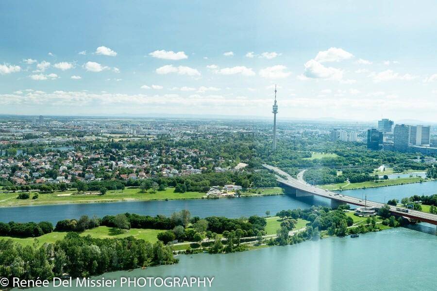 Weitläufiger Luftbildblick auf die Stadt mit Fluss, Brücken und grünen Landschaften unter blauem Himmel.