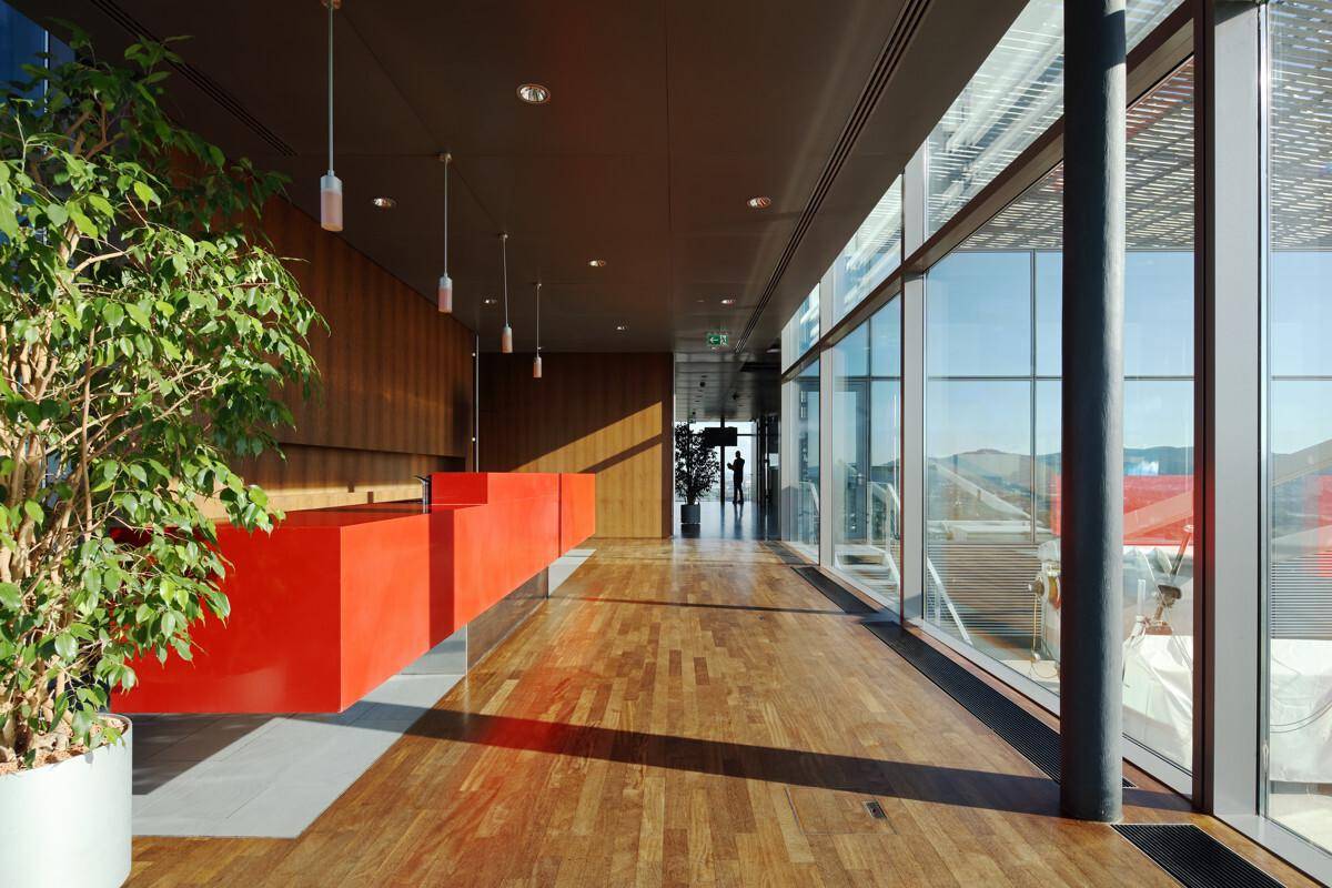 Heller Bürogang mit Holzboden, roter Rezeption und großen Fenstern mit Blick nach draußen.
