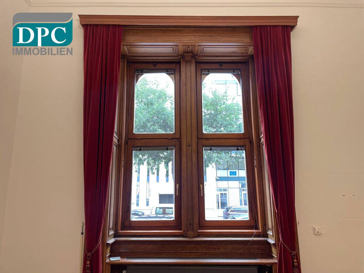 Detailansicht eines großen Holzfensters mit roten Vorhängen, das viel Tageslicht hereinlässt und eine traditionelle Ästhetik zeigt.