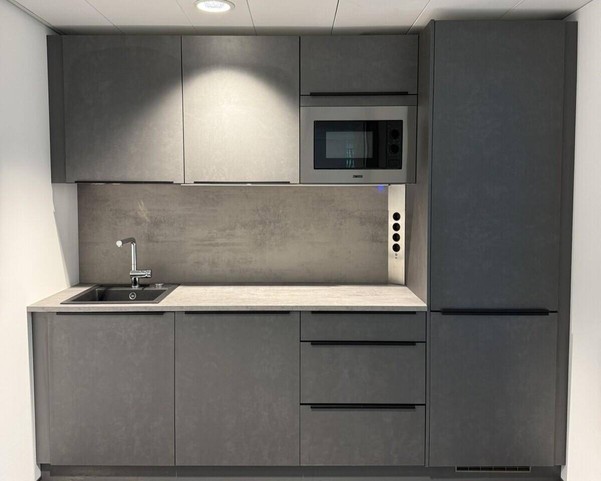 Moderne Küchenzeile in Grau mit integrierter Mikrowelle, Spüle und Kühlschrank.