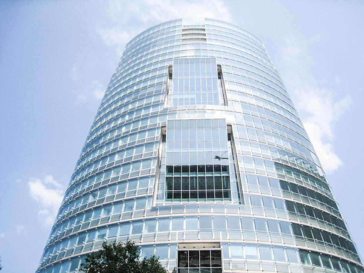 Architektonisch beeindruckendes Hochhaus mit glänzender Glasfassade unter blauem Himmel.