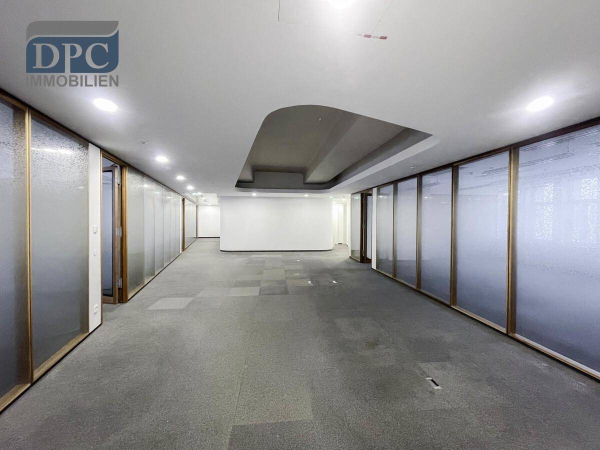 Langer Bürogang mit Glaswänden und Einbauleuchten, der eine moderne und offene Arbeitsumgebung schafft.