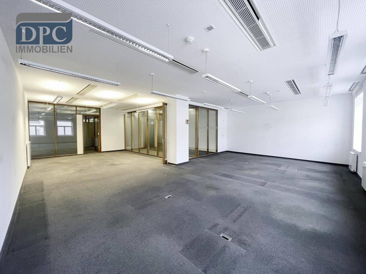 Weiterer Blick auf den geräumigen Bürobereich mit grauem Teppich, weißen Wänden und flexiblen Glasabtrennungen.