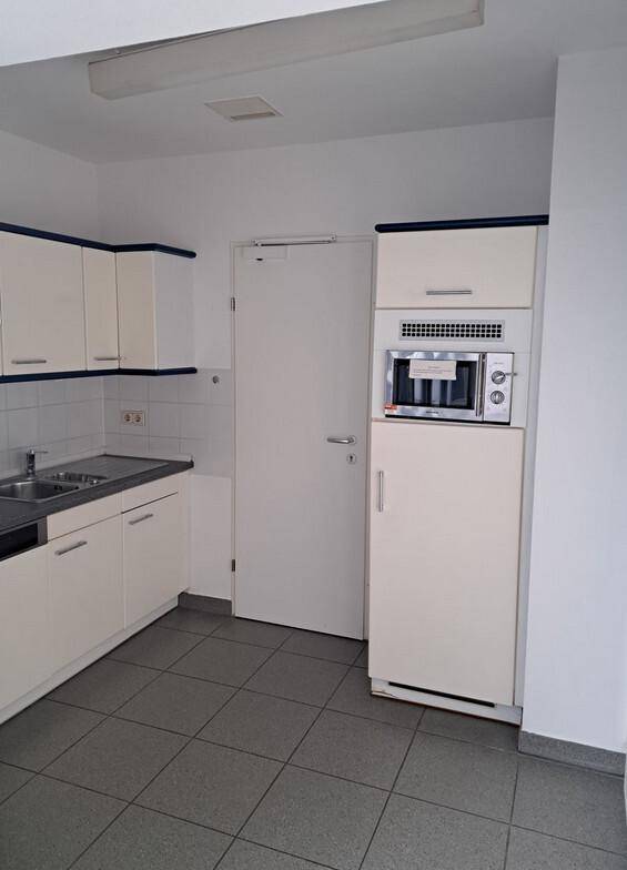 Funktionale Küche mit weißen Einbauschränken, integrierter Mikrowelle und Kühlschrank sowie Fliesenboden.