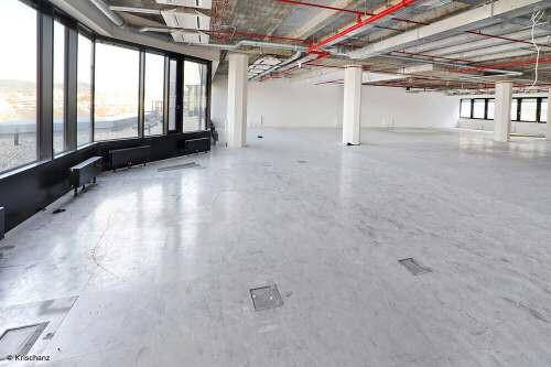 Weitläufiger, unmöblierter Bürobereich im Rohbau mit Betonboden und großen Fenstern, die viel Licht spenden.