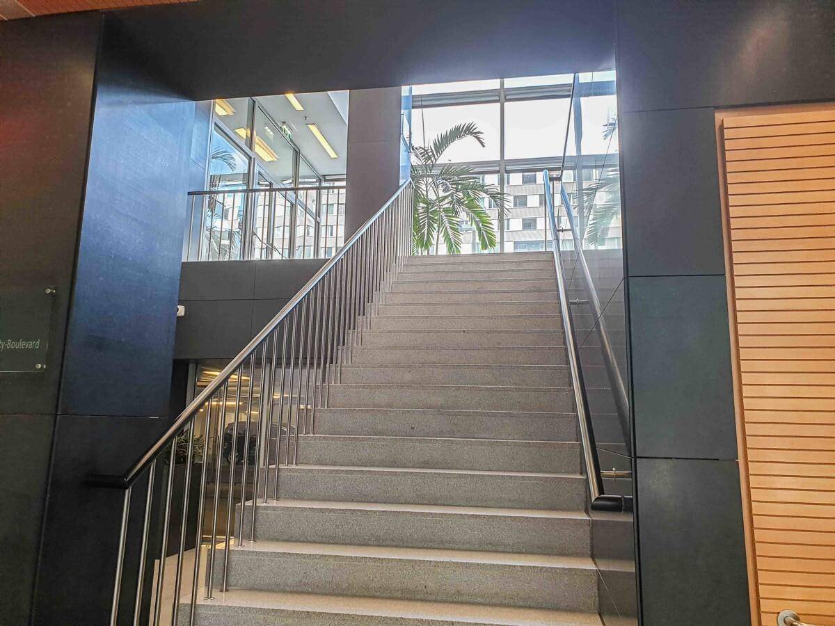 Elegante Treppe mit Edelstahlgeländer und großen Fenstern, die viel Licht hereinlassen und eine offene Gestaltung bieten.