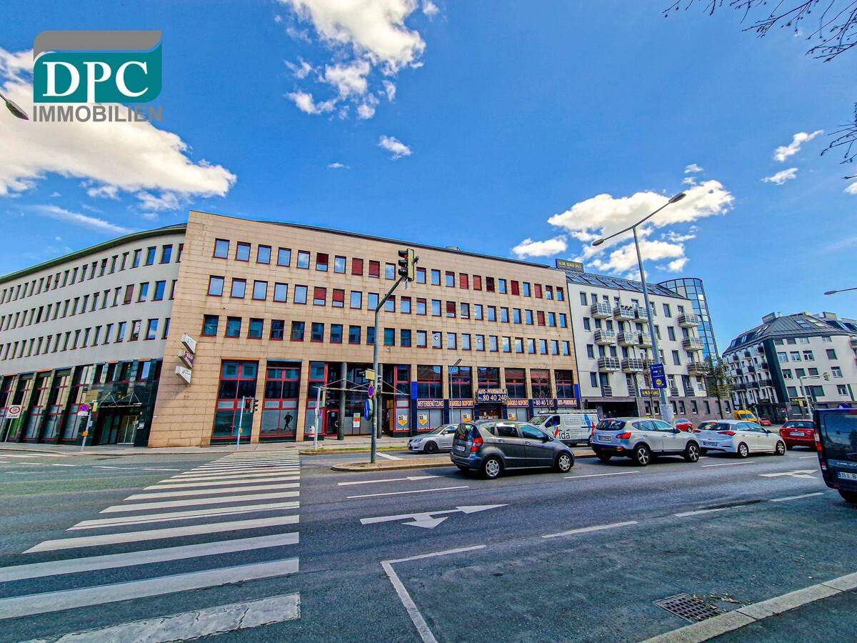 Weitwinkelaufnahme des modernen Bürokomplexes an einer belebten Straße mit weiteren Gebäuden im Hintergrund.