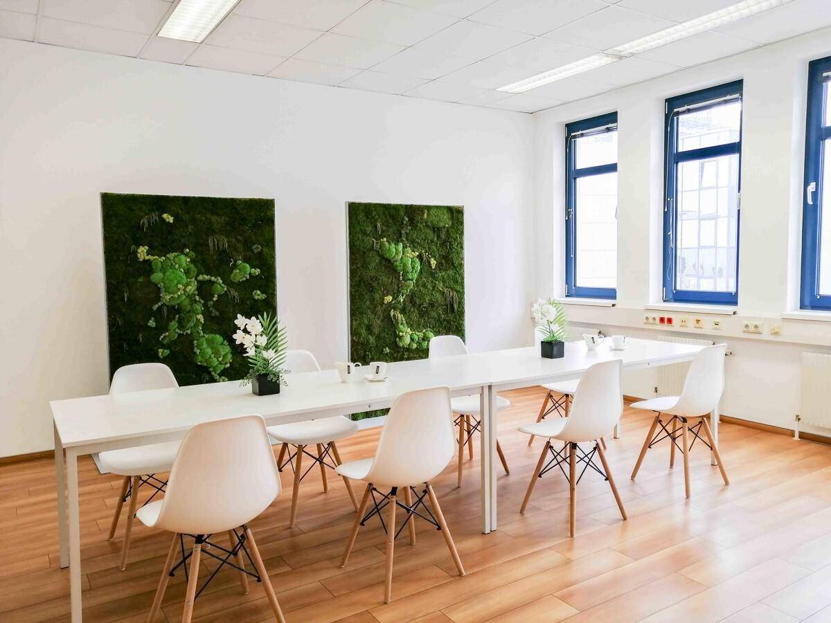 Heller Konferenzraum mit Holzboden, langen Tischen und dekorativen Mooswänden.