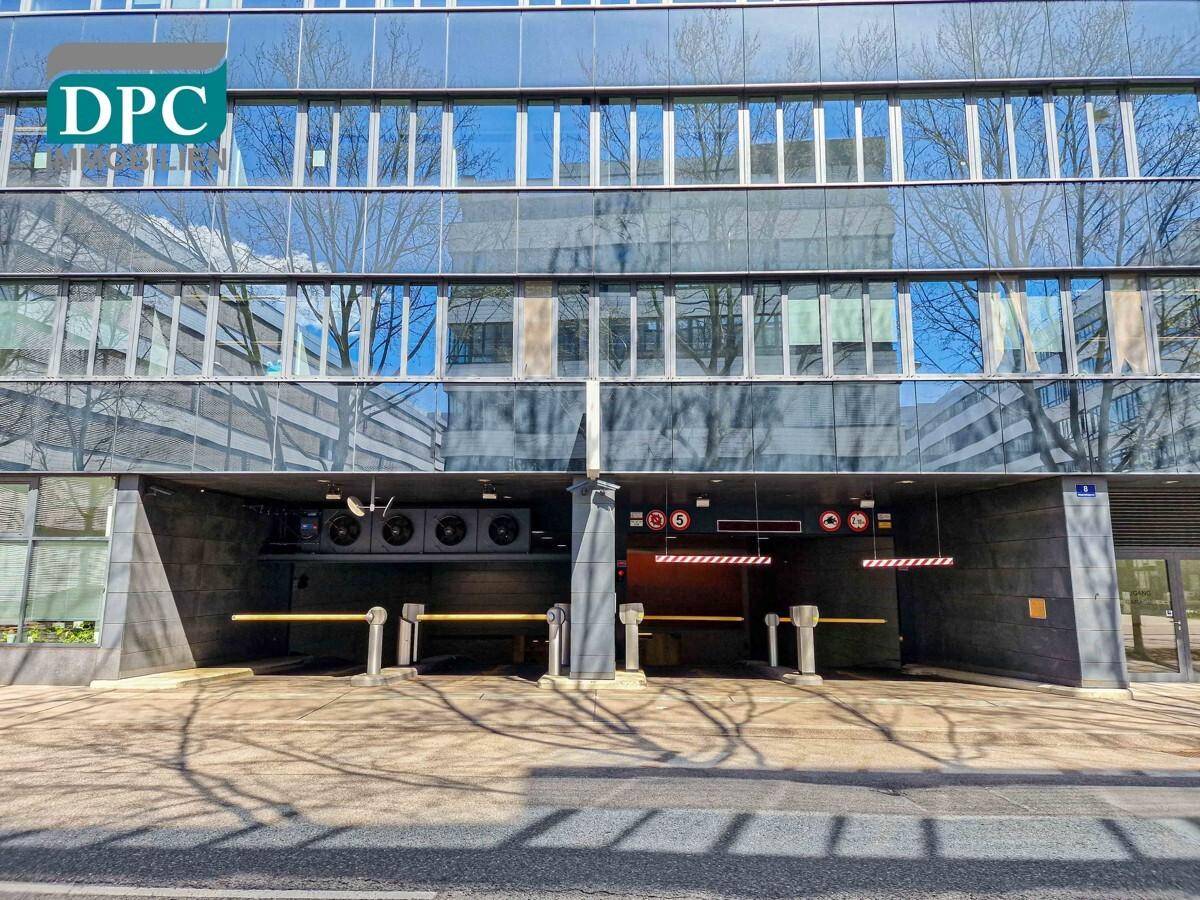 Eingang zu einer Tiefgarage unter einem modernen Bürogebäude mit Glasfassade und Überwachungstechnik.