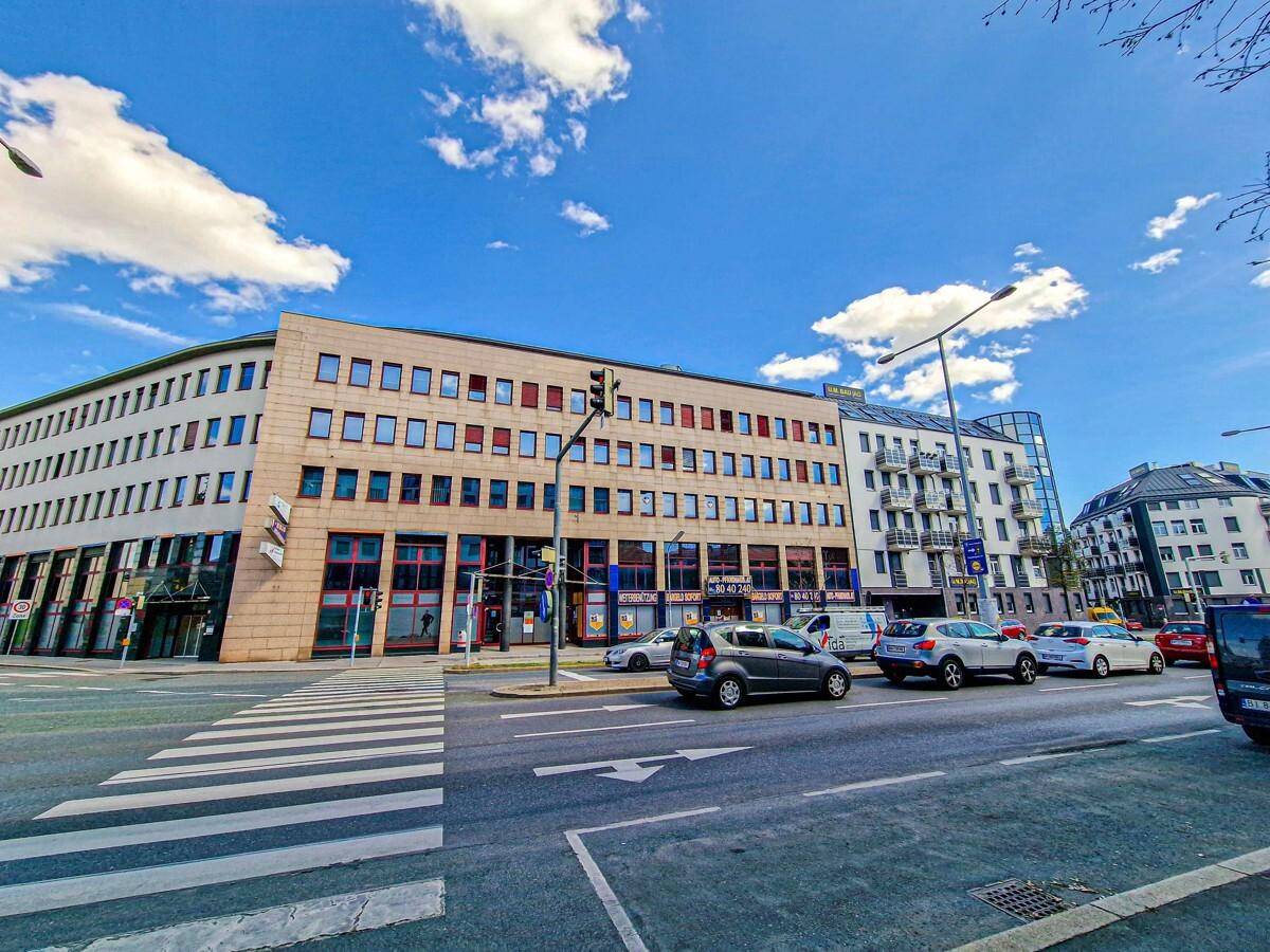 Weitwinkelaufnahme des modernen Bürokomplexes an einer belebten Straße mit weiteren Gebäuden im Hintergrund.