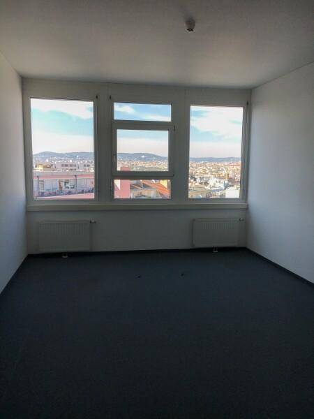 Heller Büroraum mit großen Fenstern, die einen weiten Blick über die Stadt ermöglichen, und einem dunklen Teppichboden.