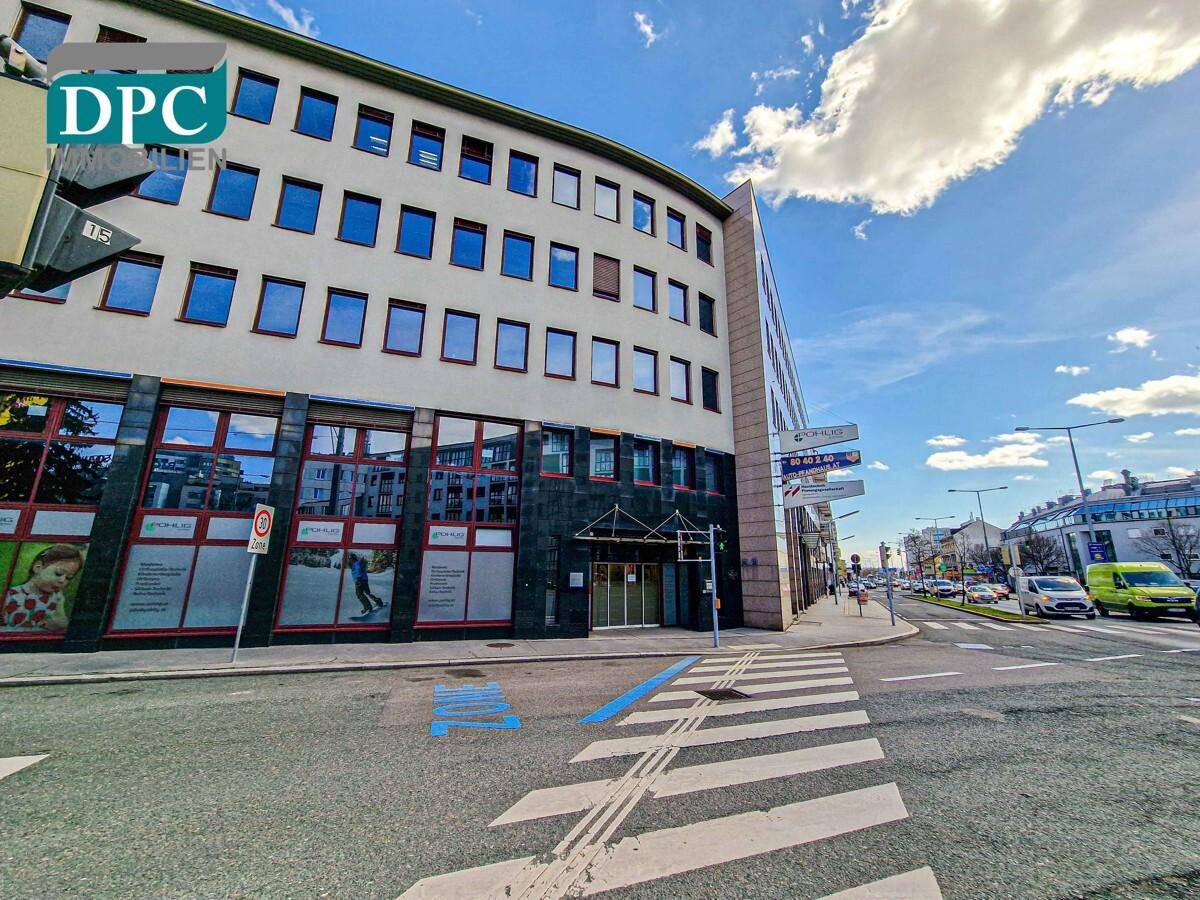 Modernes Bürogebäude an einer Straßenecke mit großen Fenstern und einer dunklen Fassadenverkleidung.