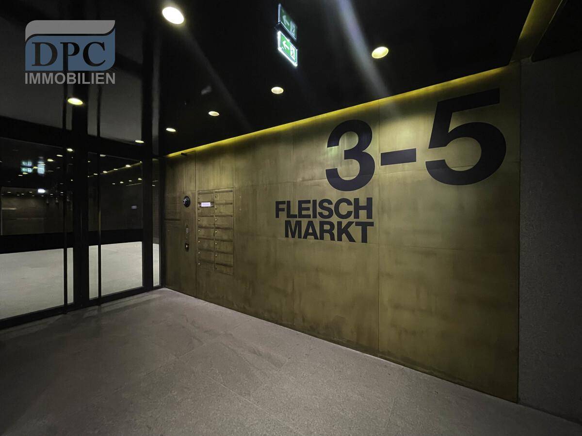 Moderner Eingangsbereich mit einer großen goldenen Wand, Hausnummer und Postfächern, stilvoll beleuchtet.