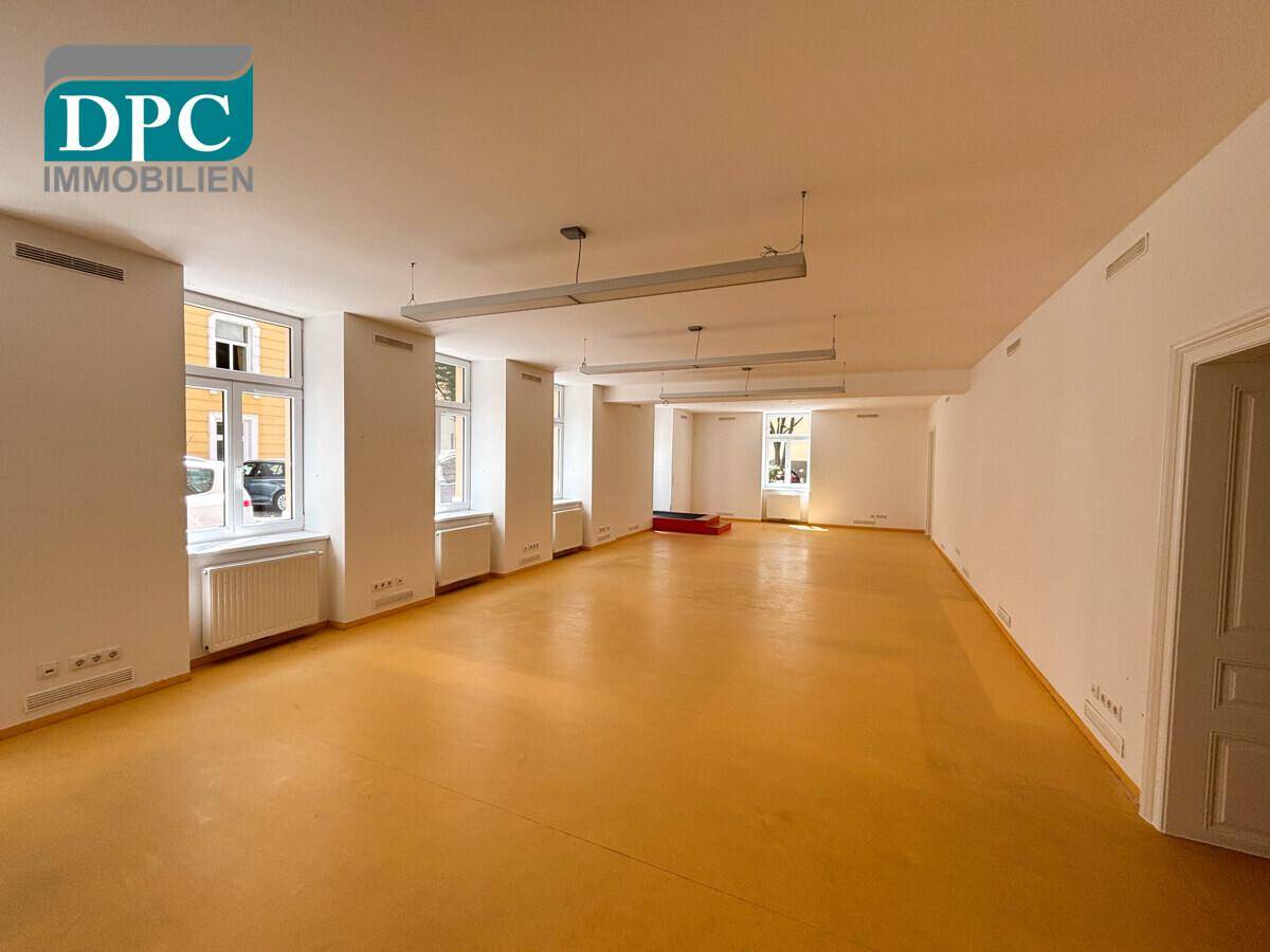 Großer, leerer Raum mit vielen Fenstern und gelbem Boden, ideal für ein Büro oder Geschäft.