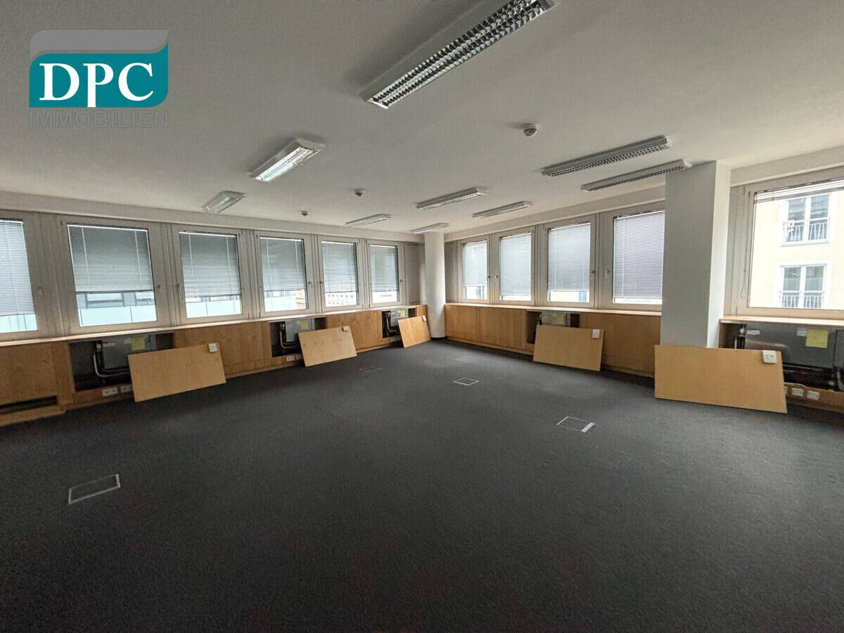 Weitläufiges Büro mit Teppichboden, zahlreichen Fenstern mit Jalousien und Holzverkleidungen.