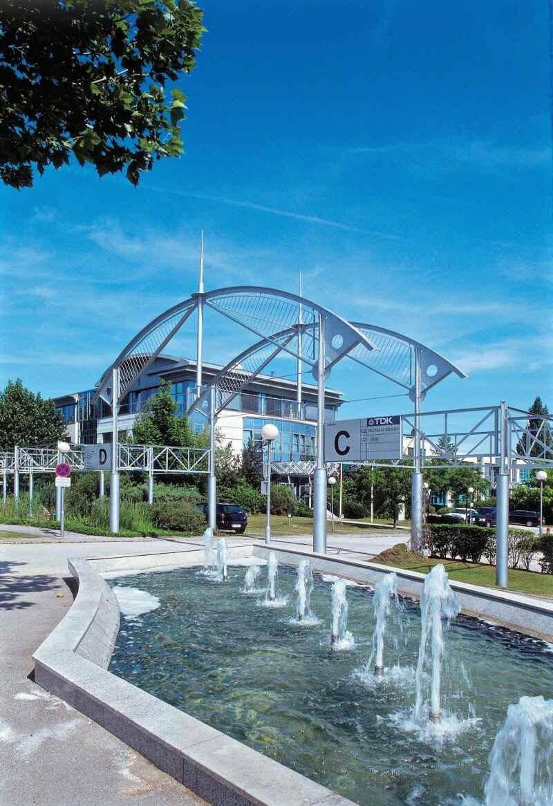 Springbrunnenanlage im Freien vor einem modernen Bürogebäude mit blauen Himmel und Bäumen.