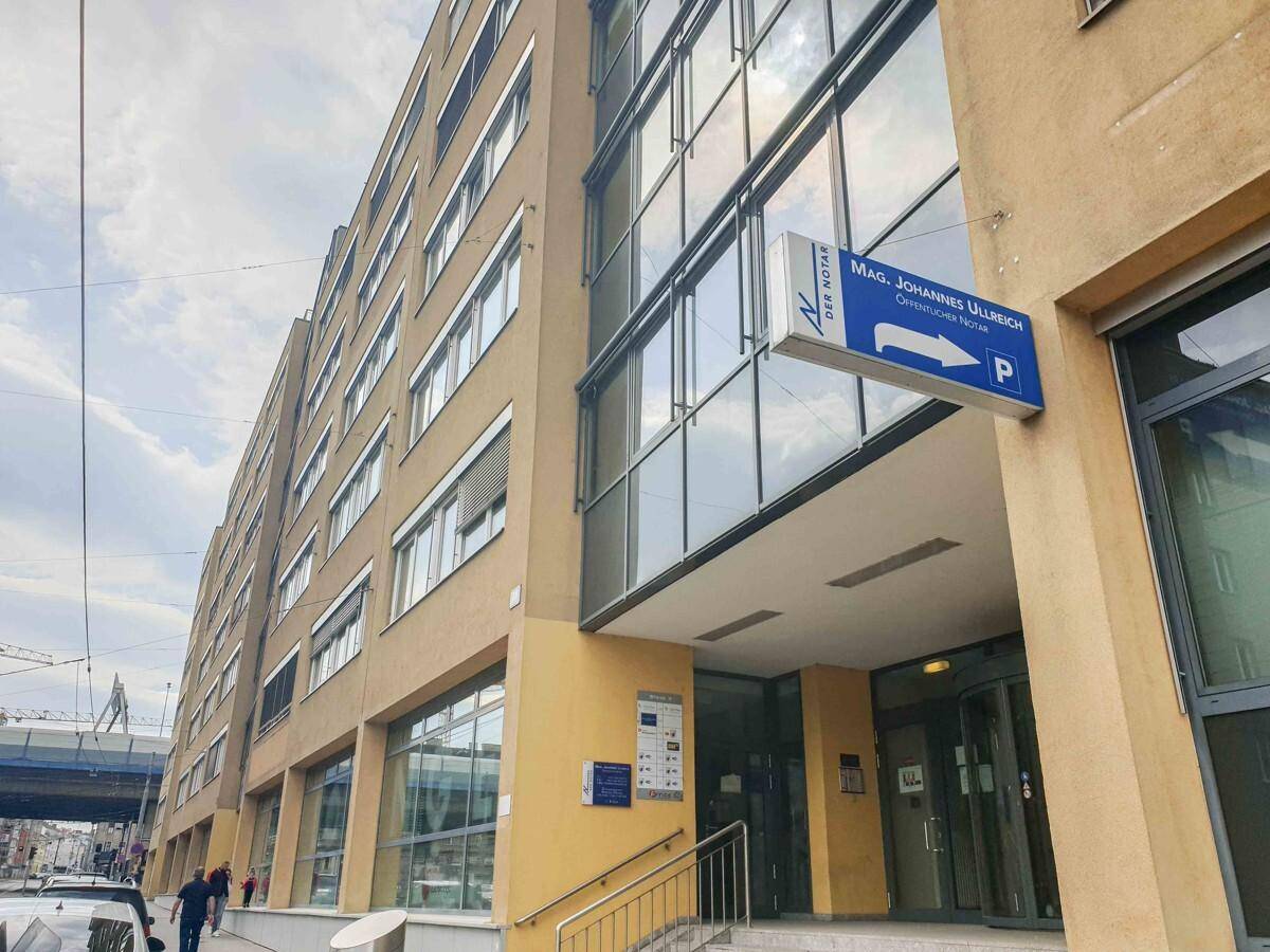 Eingangsbereich eines modernen Bürogebäudes mit großen Glasflächen und Hinweisschildern.