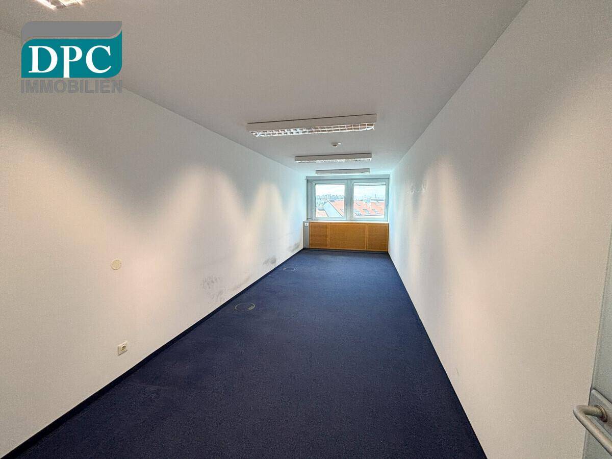Kleineres Büro mit blauem Teppichboden und einem Fenster, geeignet für Einzelarbeitsplätze oder Besprechungen.