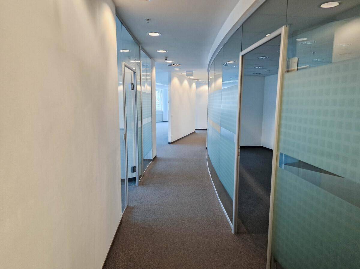 Moderner Büroflur mit Teppichboden und Glaswänden, die einzelne Büros abtrennen und Transparenz schaffen.