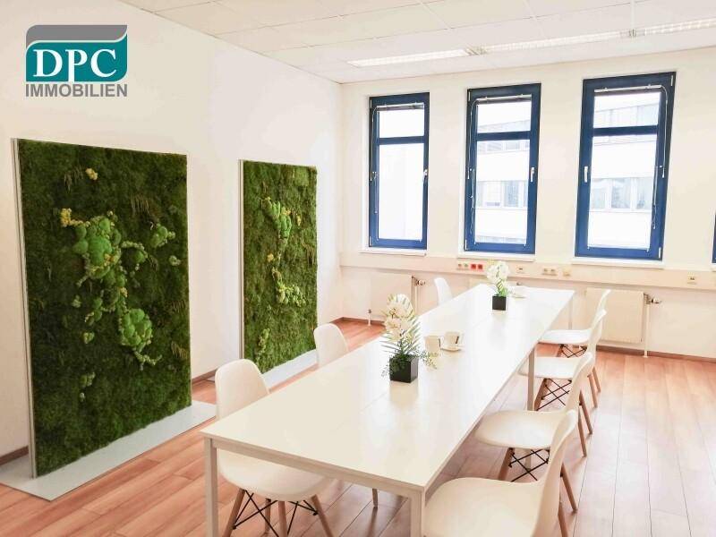 Heller Konferenzraum mit Holzboden, langen Tischen und dekorativen Mooswänden.
