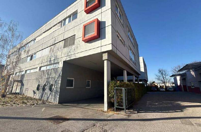 Seitenansicht eines modernen Bürogebäudes mit markanten roten Akzenten und überdachten Parkbereichen.