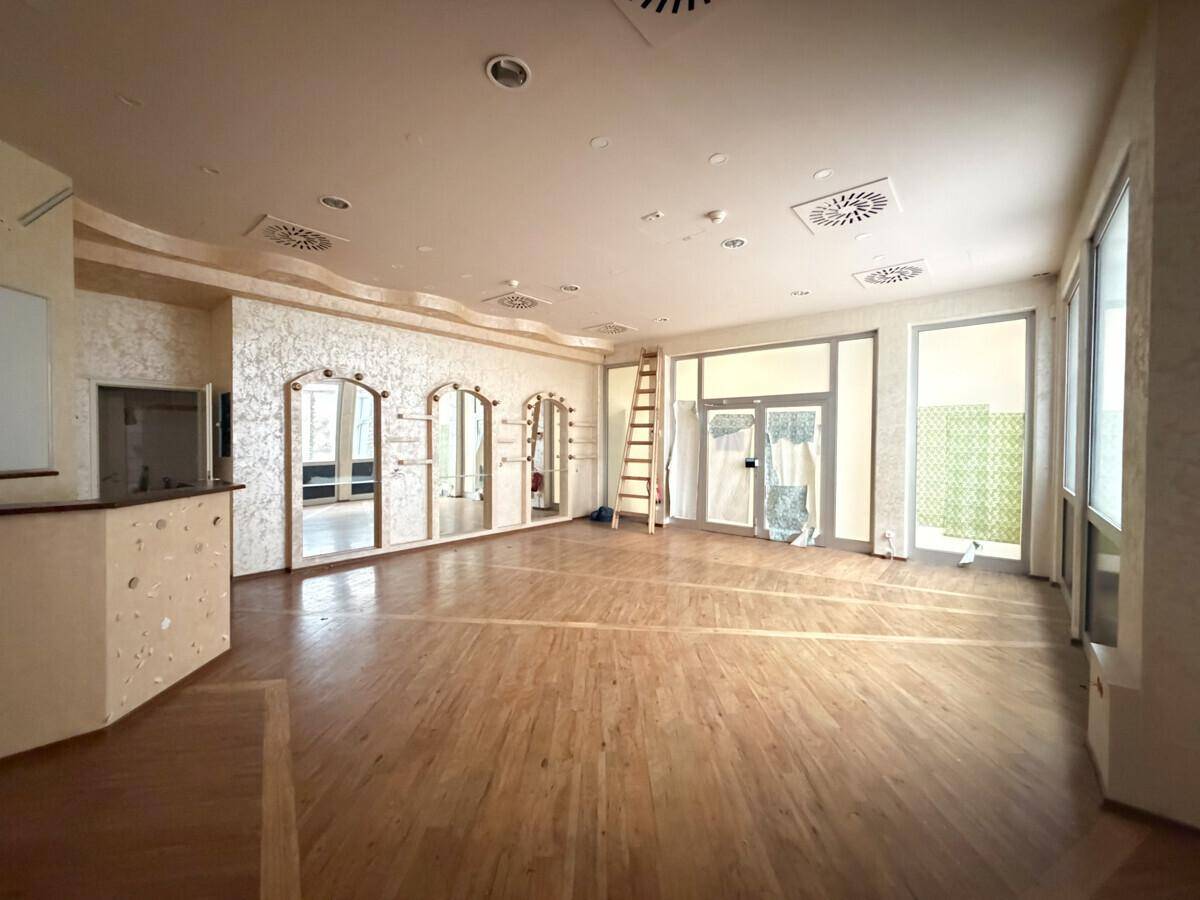 Geräumiger Gewerberaum mit Holzboden, strukturierten Wänden und großen Fenstern, ideal für Einzelhandel oder Büro.