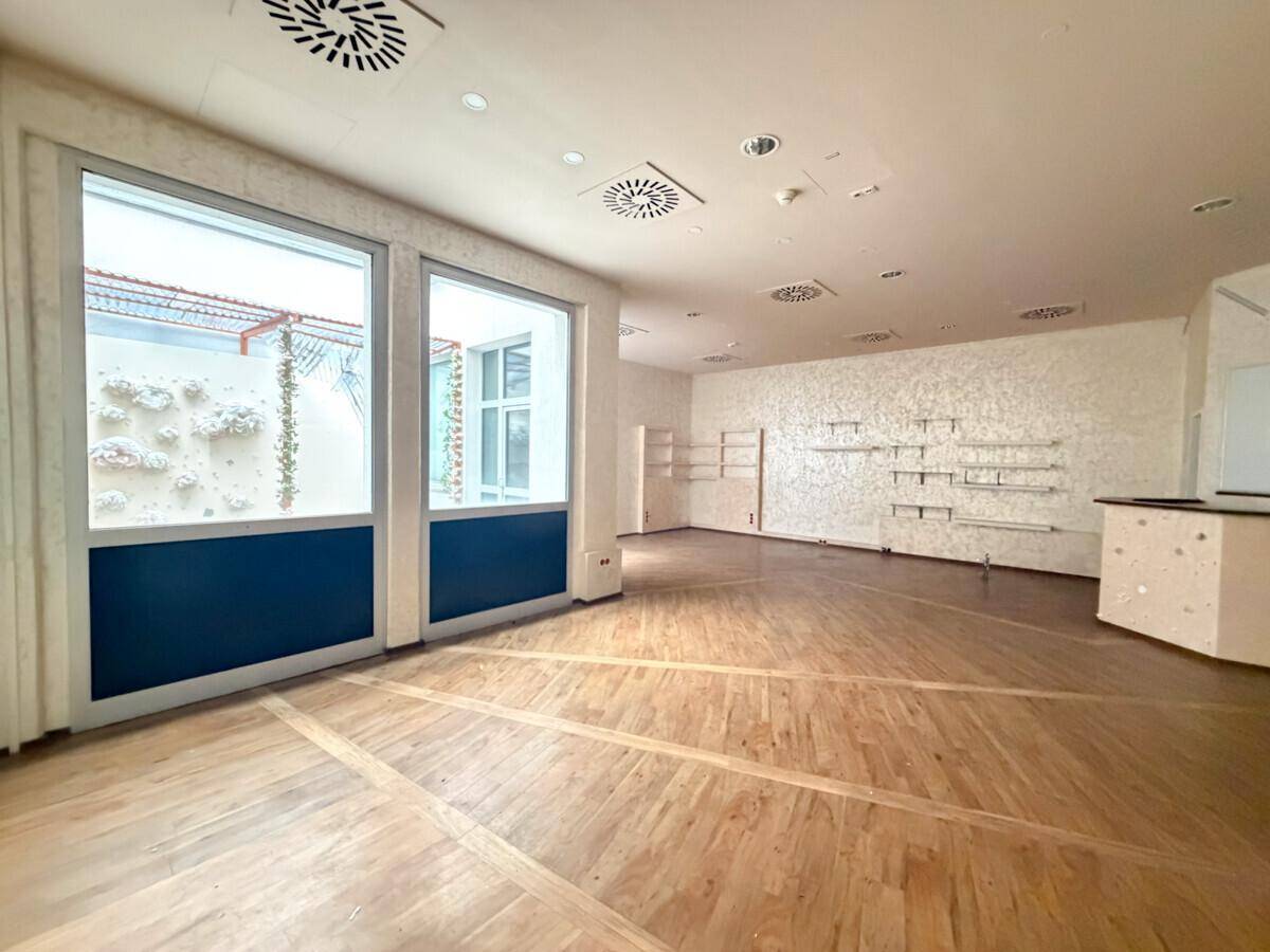 Heller Gewerberaum mit Holzboden, großen Fenstern und Regalsystemen an den strukturierten Wänden.