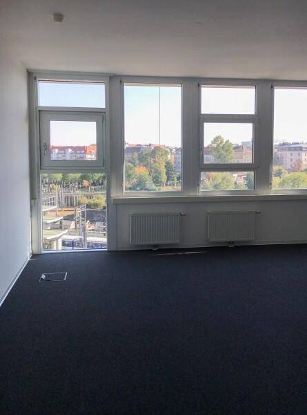 Heller Büroraum mit großen Fenstern, die einen weiten Blick über die Stadt ermöglichen, und einem dunklen Teppichboden.