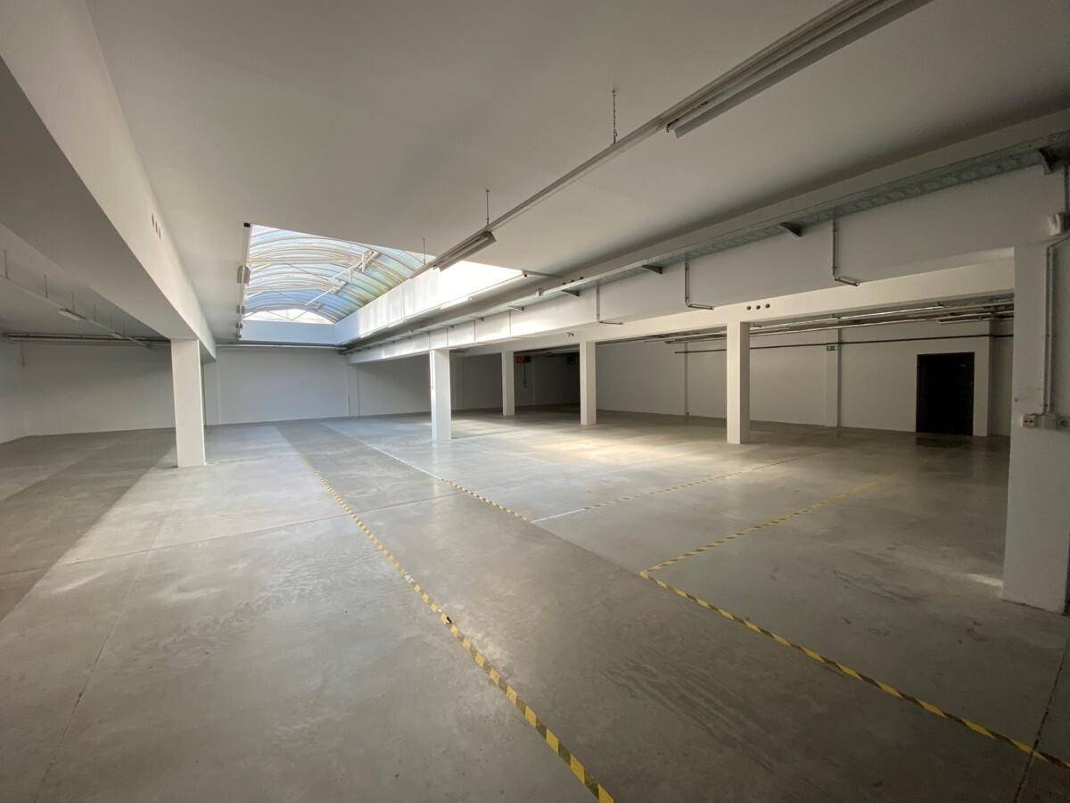 Heller Gewerberaum mit Betonboden, Säulen und einem großen Oberlicht für viel Tageslicht.