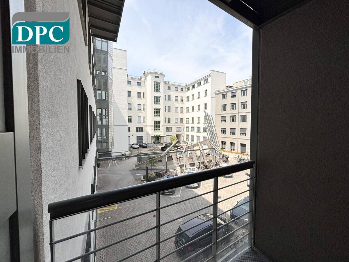 Blick von einem Balkon in einen modernen Innenhof mit Parkplätzen und umliegenden Gebäuden.
