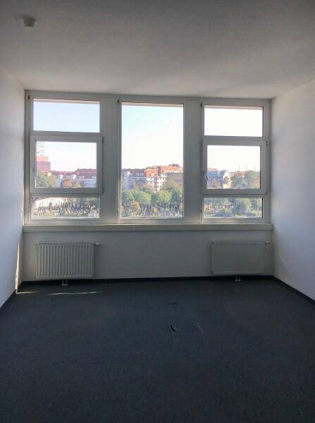 Heller Büroraum mit großen Fenstern, die einen Blick auf die Stadt bieten, und einem dunklen Teppichboden.