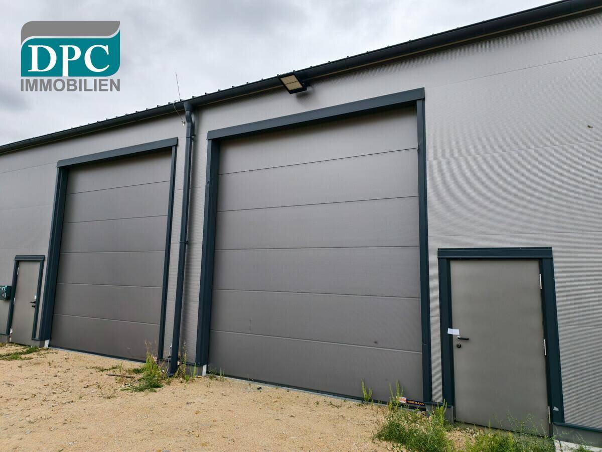 Moderne Industriefassade mit zwei großen Rolltoren und separaten Zugangstüren für effiziente Logistik.