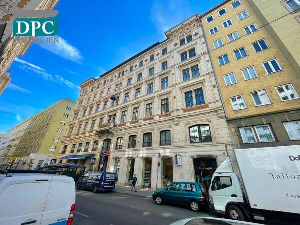 Historisches Gebäude an einer belebten Straße mit Geschäften und anderen Gebäuden unter blauem Himmel.
