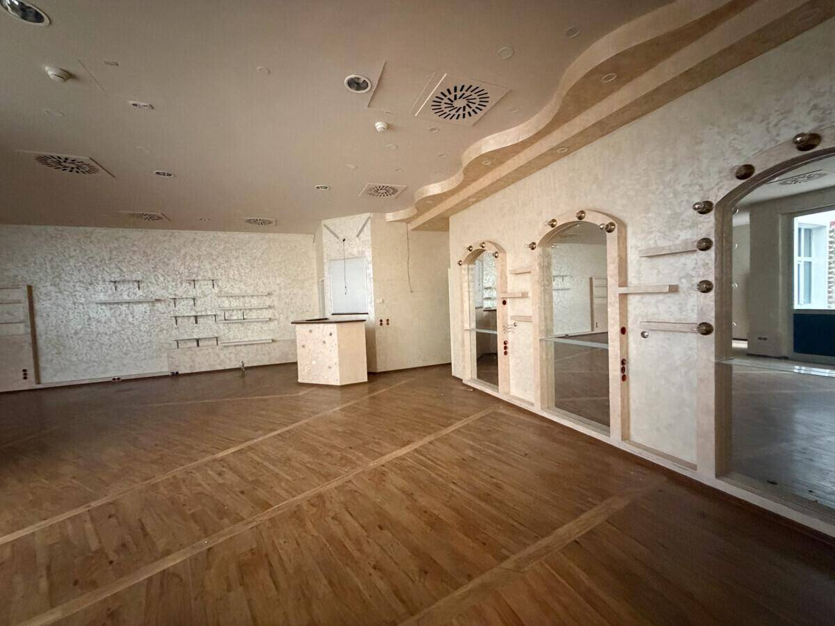 Geräumiger Gewerberaum mit Holzboden, strukturierten Wänden, Spiegeln und einem Holztresen.
