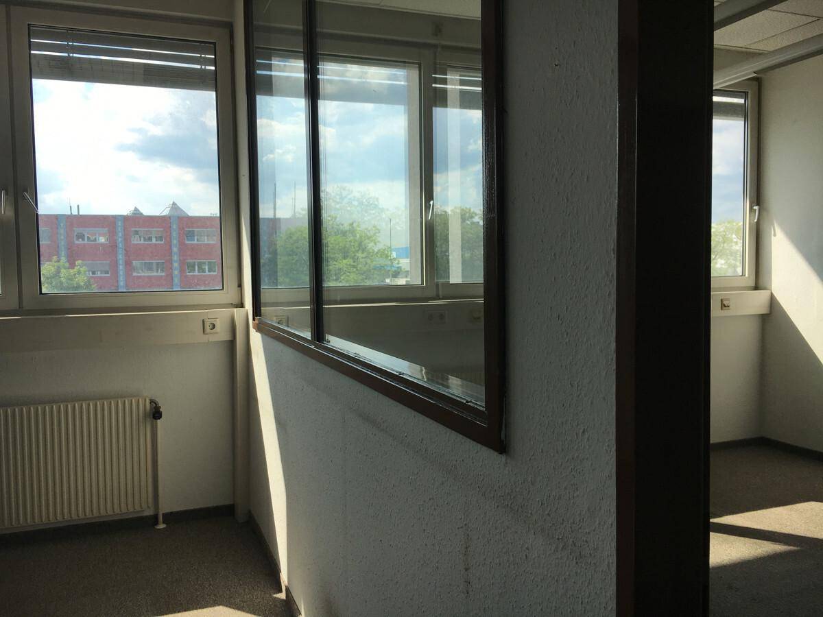 Heller Bürobereich mit großen Fenstern und einer Glasabtrennung, die den Raum in natürliches Licht taucht.