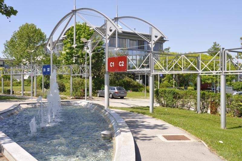 Ein Springbrunnen im Außenbereich eines Geschäftsparks mit modernen Metallstrukturen und Gebäuden im Hintergrund.