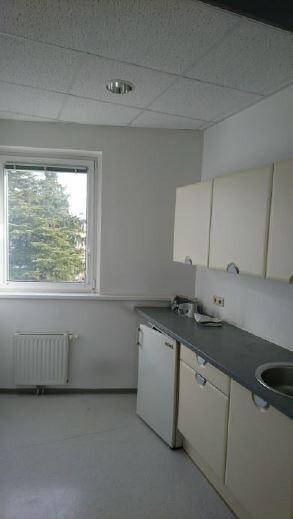 Kleine Küchenzeile mit weißen Schränken, Spüle und Fenster, ideal für eine Teeküche.