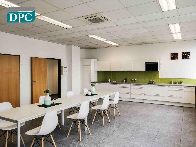 Geräumige Teeküche mit langer Tafel, weißen Schränken und grüner Rückwand.