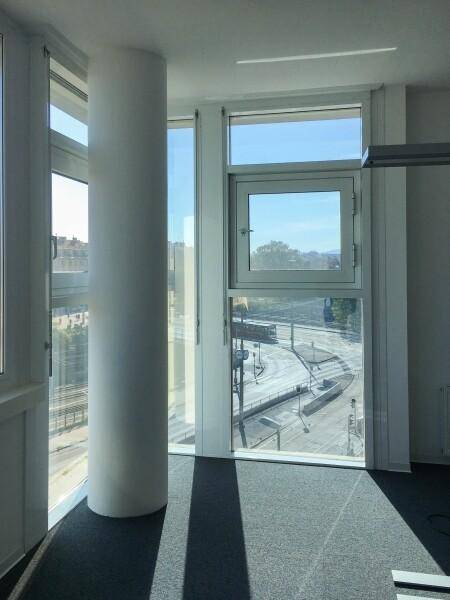 Heller Büroraum mit einer Säule und großen Fenstern, die einen Blick auf Bahngleise und die Stadt bieten.
