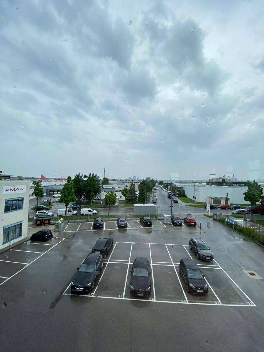 Blick aus dem Fenster auf einen Parkplatz und eine Straße an einem bewölkten Tag mit Regentropfen auf der Scheibe.