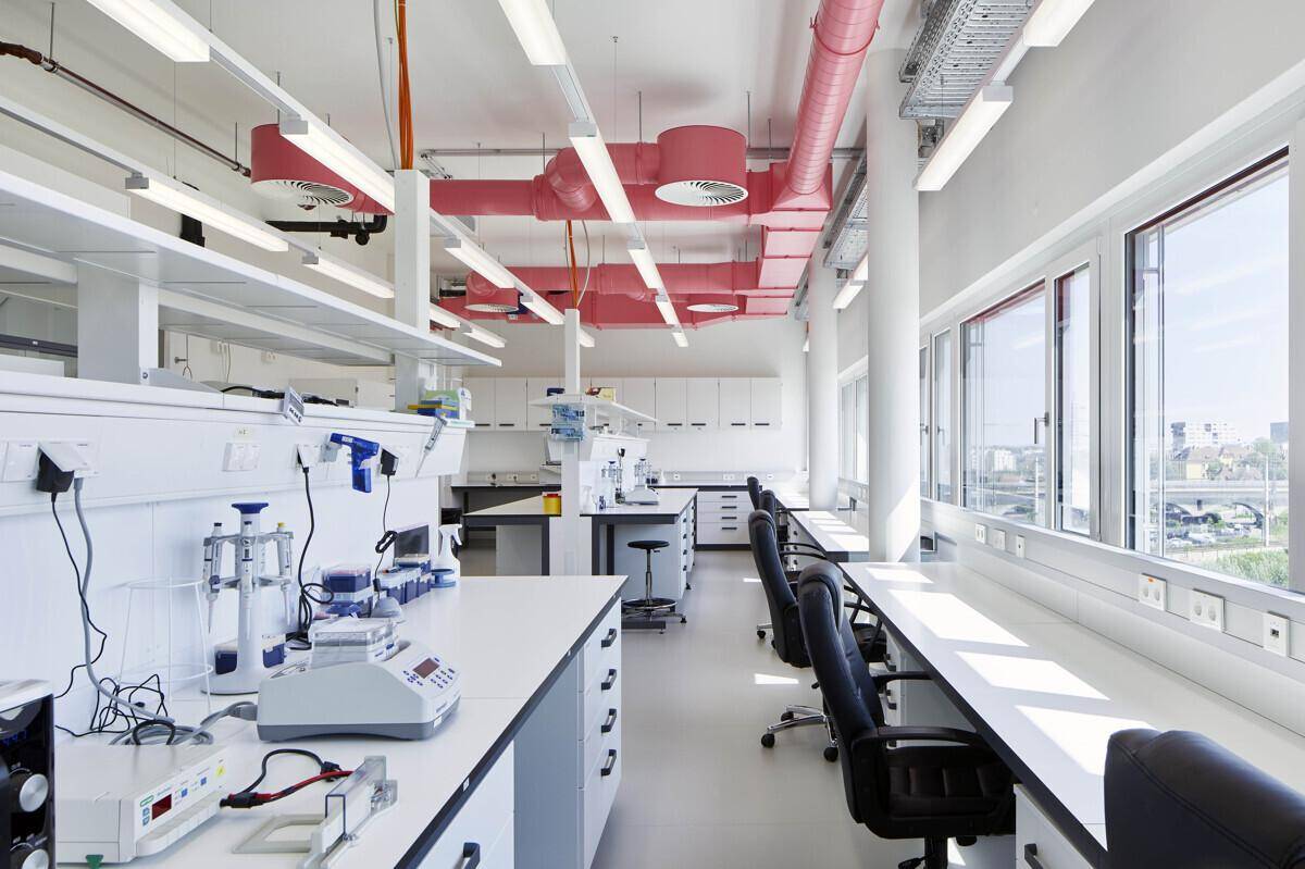 Funktionales Labor mit Arbeitsflächen, Geräten und auffälligen roten Lüftungsrohren unter der Decke.