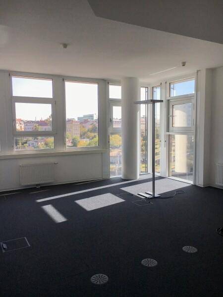 Geräumiger Bürobereich mit einer Säule, großen Fenstern und einem dunklen Teppichboden, der viel Sonnenlicht empfängt.