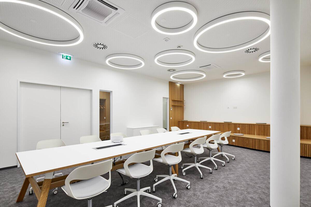 Moderner Konferenzraum mit einzigartigen runden Deckenleuchten, Holzakzenten und einem langen Besprechungstisch.