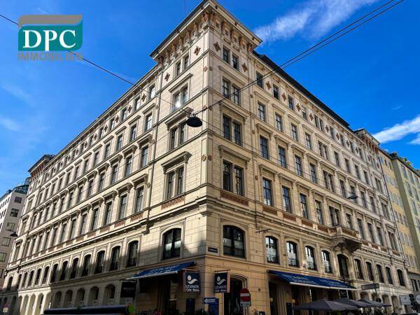 Historisches Eckgebäude mit reich verzierter Fassade und Geschäften im Erdgeschoss unter blauem Himmel.