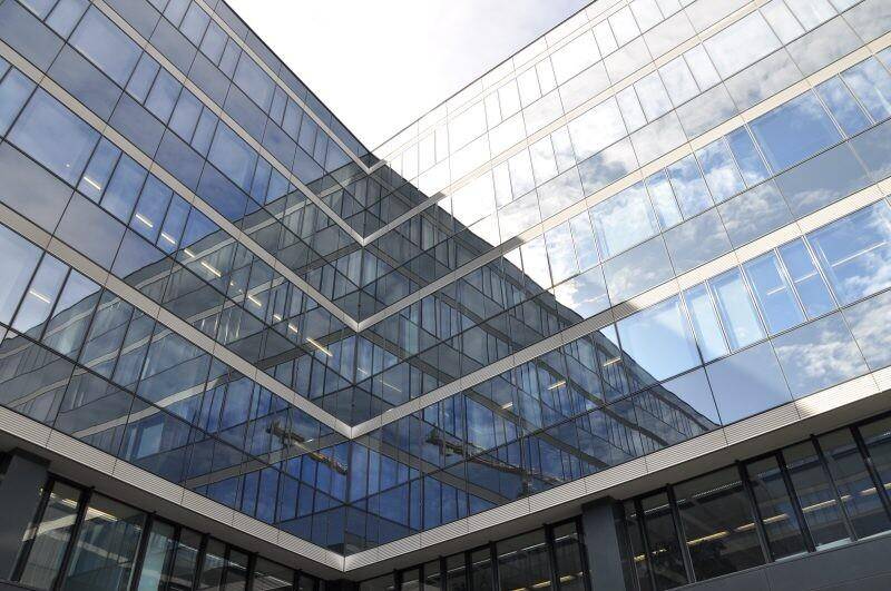 Moderne Glasfassade eines Bürogebäudes, die den Himmel und Wolken in ihren reflektierenden Oberflächen widerspiegelt.