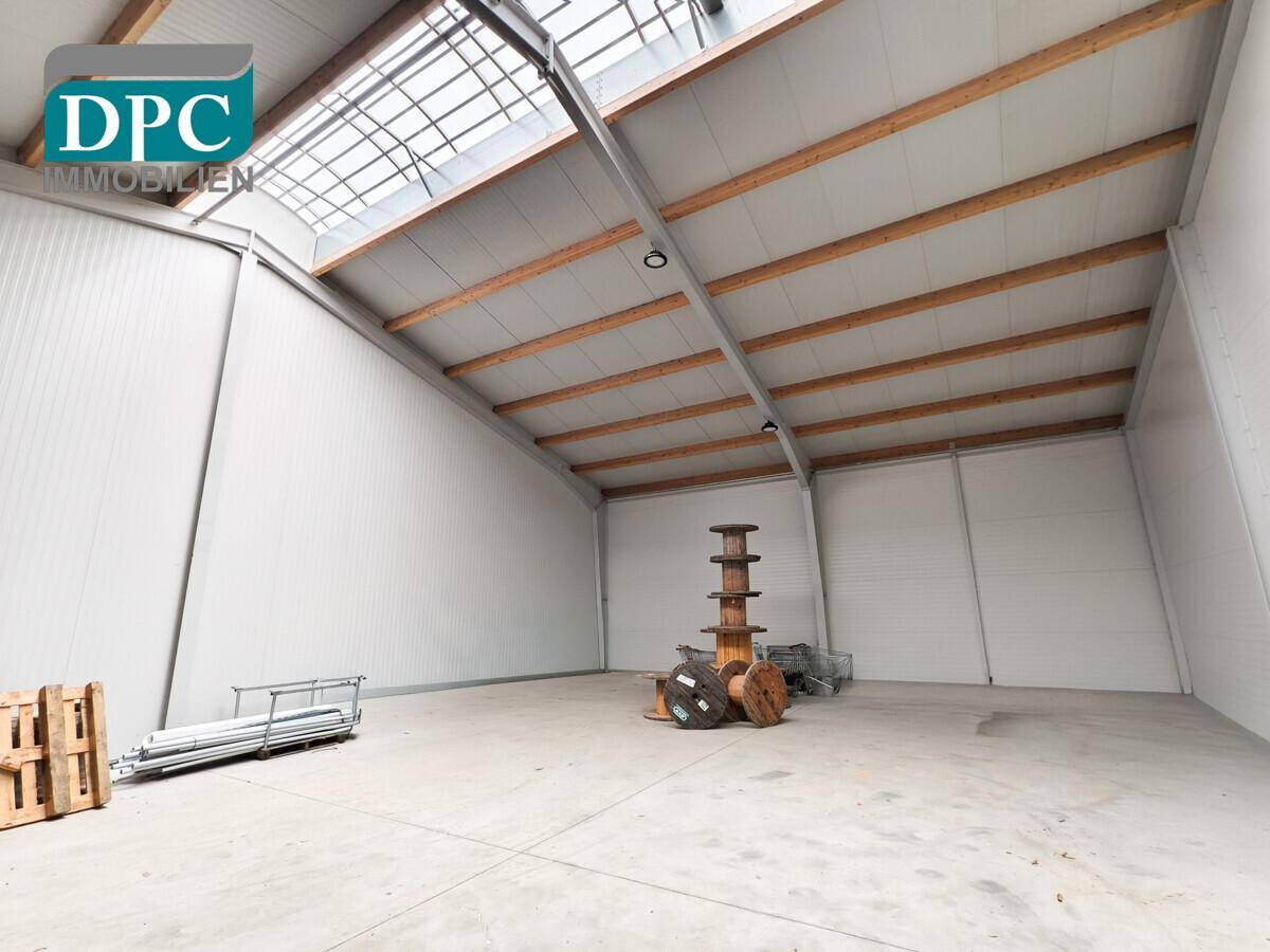 Helle und offene Lagerhalle mit Betonboden und sichtbaren Dachbalken, ideal für Produktion oder Lagerung.
