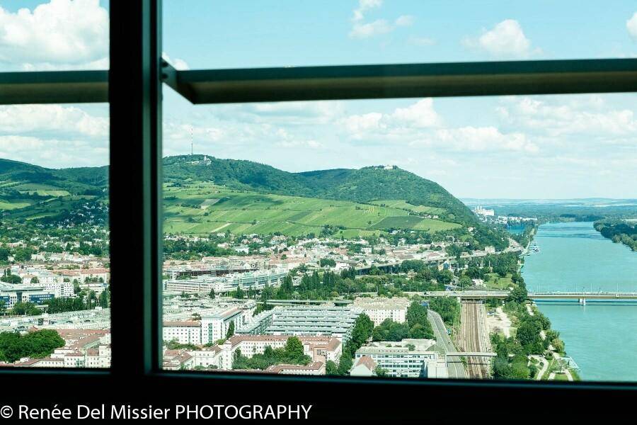 Panoramablick aus einem Fenster auf eine Stadt, Fluss, grüne Hügel und eine Brücke.